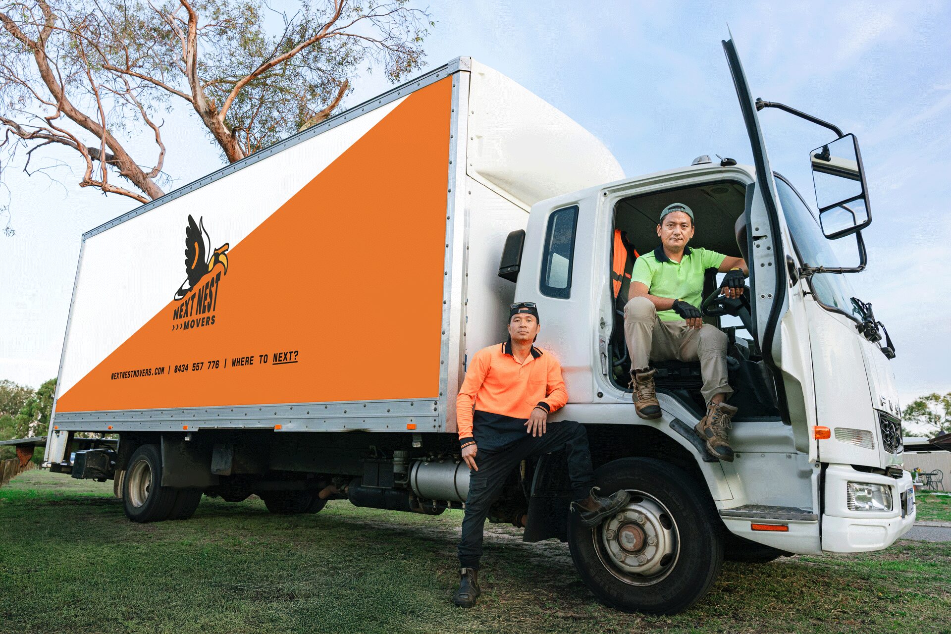 Professional photo of moving truck with two movers. One is sitting half our in the cab the other leaning on the truck. Truck covered in custom Next Nest Movers livery.